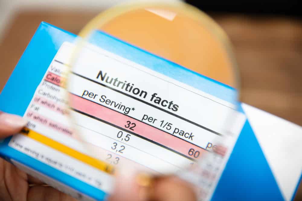 woman looking nutrition facts on food box through magnifying glass