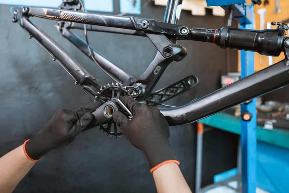 a mechanic's hand wearing gloves installing the right crank arm on the bottom bracket with a workshop background