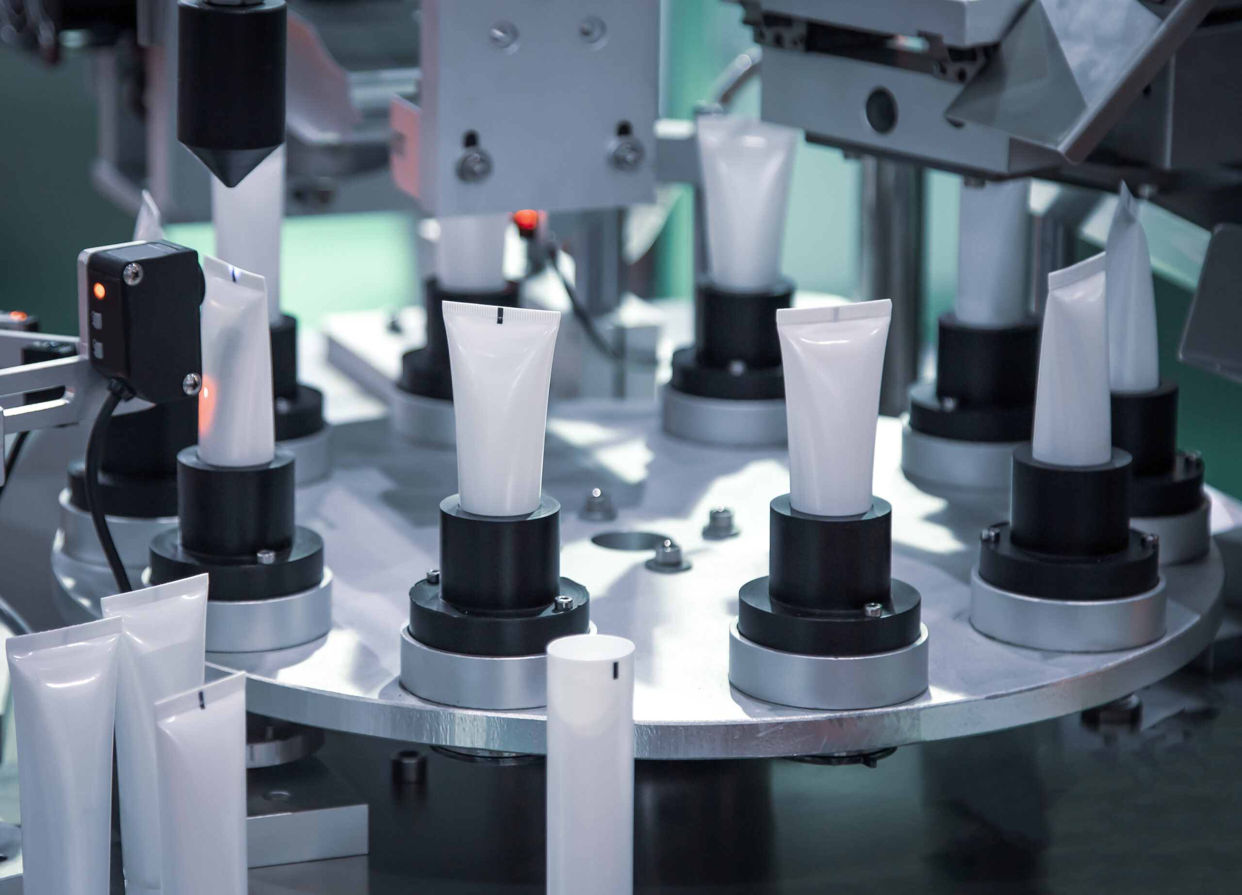A close-up of a high-speed automated filling machine organizing white cosmetic tubes on a rotating platform in a clean factory environment. This demonstrates how AI vision is used in the cosmetics industry for precise quality inspection of packaging, fill levels, sealing, and labeling.