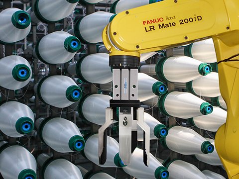 Yellow FANUC LR Mate 200iD robot using a gripper to perform automated deracking of textile yarn bobbins or spools from a densely packed rack, guided by AccuPick AI vision.